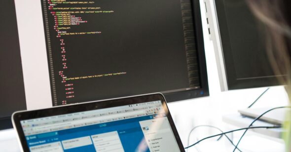 Programmer working on code across multiple screens in a modern office setting.